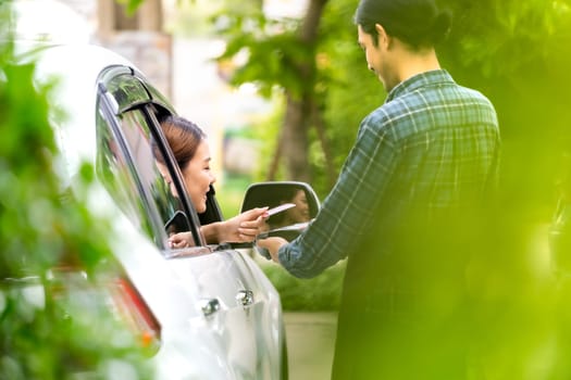 Back view of asian woman customer make mobile payment contactless technology on drive thru food service restaurant while picking up. Drive through is more popular after coronavirus covid-19 pandemic.