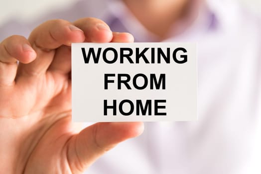 Closeup on businessman holding a card with text Working From Home, business concept image with soft focus background