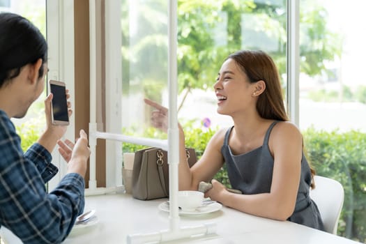 Asian young couple eating out together at new normal social distance restaurant with table shiled partition reduce infection of coronavirus covid-19 pandemic. Restaurant new normal lifestyle.