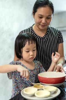 Asian girl cooking egg tart bakery with her mom, housework for child make executive function for kid. Houseworking food lifstyle and family concept.