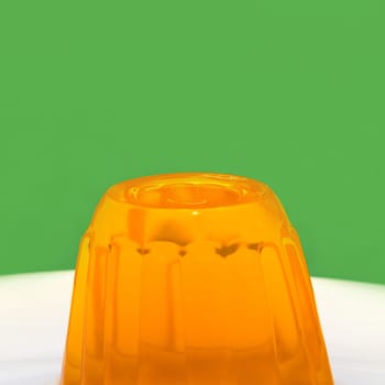 Close up of a orange gelatin on a white plate. Green background.