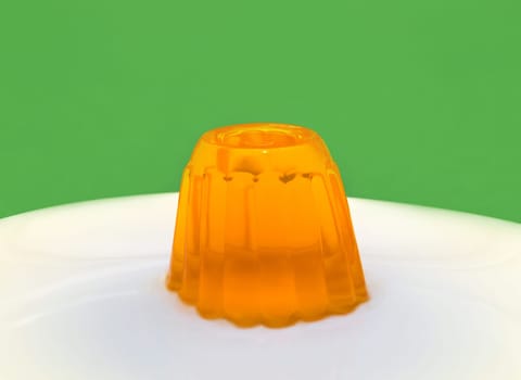 Close up of a orange gelatin on a white plate. Green background.