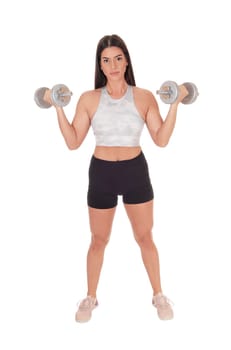 A beautiful young woman standing in shorts and sports bra from the.front lifting her two dumbbells, isolated for white background.