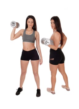 Two young beautiful woman standing in workout outfits in the studio.working out with there dumbbells, isolated for white background.