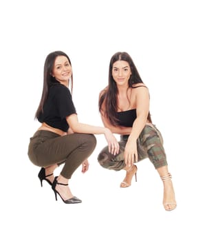Two beautiful young woman crouching side by side in jeans and heels.looking at the camera, isolated for white background.