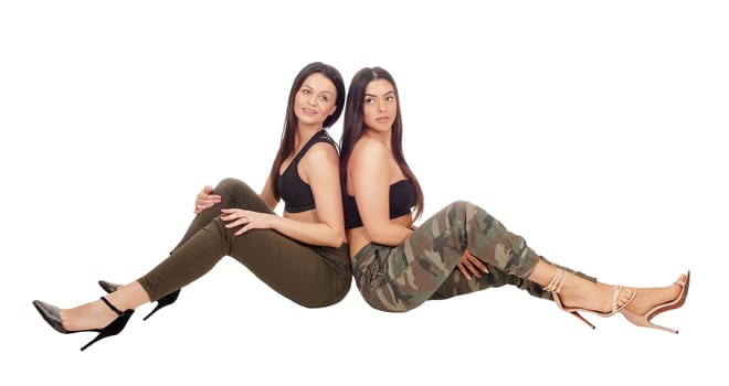 Two beautiful young woman sitting side by side in jeans and heels.looking at the camera, isolated for white background.
