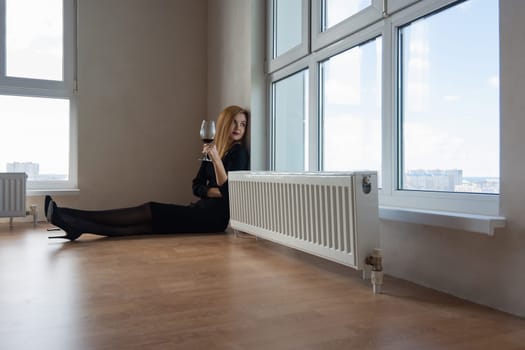 girl thoughtfully stares into a large window with a glass of wine in her hand