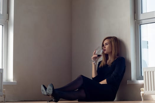 Girl drinks wine sitting on the floor near large windows