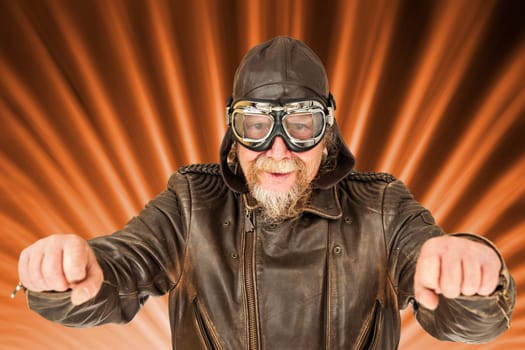 Image composition with a frontal upper body view of an older man in a brown, worn motorcycle jacket  Motorcycle cap and traditional motorcycle goggles holding an imaginary motorcycle handlebar and smiling friendly at the camera against a radially structured background.
