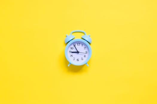 Blue alarm clock on yellow background. Flat lay. Free space for your text. Top view