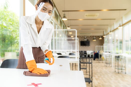 Portrait attractive asian waitress wear face mask and face shield cleaning table with alcohol and wet wipe before welcome customer. New normal hygiene restaurant concept.