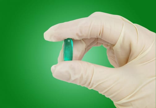 green pill in hand with medical gloves.green surface