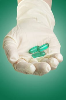 hand with medical gloves and pills on green surface