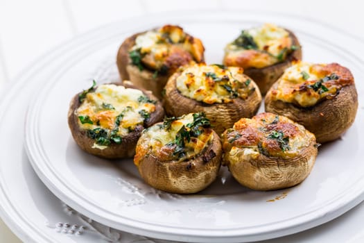 Baked champignons mushrooms, filled with cheese, parsley and roasted garlic on white plate. Selective focus. Healthy food concept.