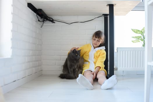 Punished girl sitting under the table and stroking a domestic cat
