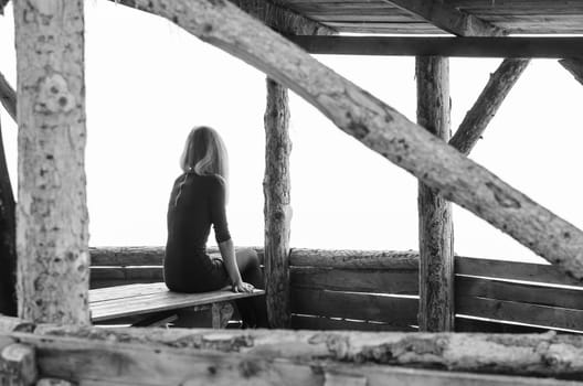 Girl alone sits early in the morning on a foggy day in a wooden arbor