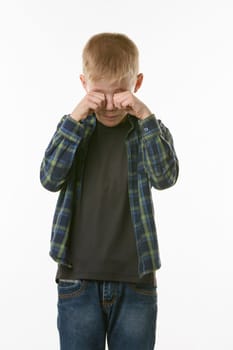 Crying boy rubs his eyes with his fists