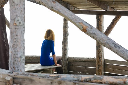 A girl sits on a table in a gazebo from a log house