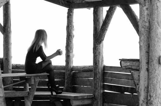 A girl sits in a wooden arbor on a foggy day and looks into the distance