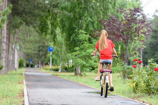 Girl in a red T-shirt rides on a bike path in the park
