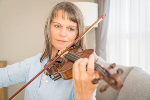 Mature woman playing violin in her urban apartment