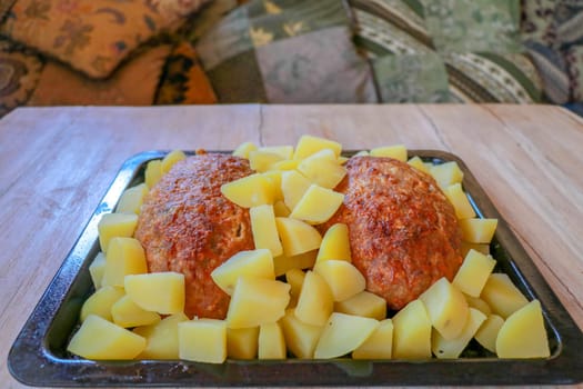 Baked minced pork and potatoes on a black baking pan. Homemade meat cutlets with potatoes in a cast iron pan served on a wooden table. Tasty and delicious lunch or dinner. Minced meat meatloaf baked.