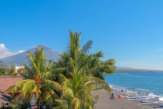 Sunset on the beach on a tropical island. Orange colored sky and clouds. Big majestic volcano on the horizon. Quiet sea and romantic atmosphere.
