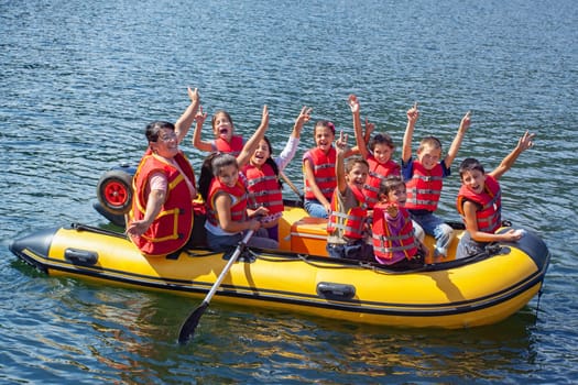 TARNITA LAKE, CLUJ COUNTY, ROMANIA - SEPTEMBER 09 2013 Children from a socially disadvantaged community taken on a holiday trip with yellow inflatable boat on the water lake, happy waving in red life jackets