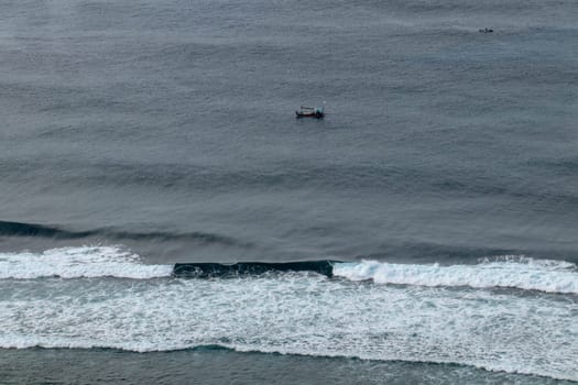 Aerial view of Nyang Nyang beach on Bali in Indonesia. A popular spot of surfers with big waves in the Indian Ocean. Fishing boats of Balinese fishermen on the sea surface. Waves break off the coast.