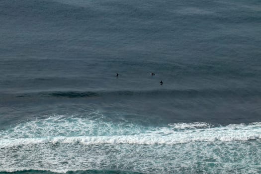 Young surfers sitting on surfboards waiting for the right wave. A young man lies on the surfboard and is spending time talking to other friends. Waves turn into sea foam as they break off the coast.