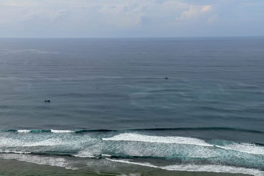 Young surfers sitting on surfboards waiting for the right wave. A young man lies on the surfboard and is spending time talking to other friends. Waves turn into sea foam as they break off the coast.