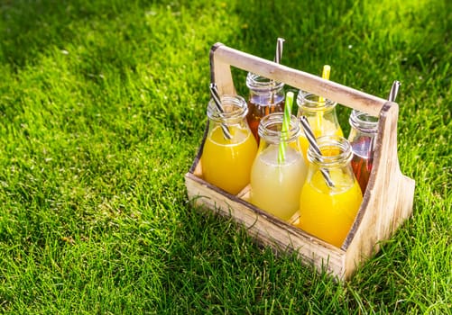 Assortment of lemonade and ice tea in bottles in wooden rack in the grass