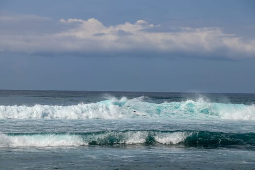 Young caucasian man surfs the ocean wave and makes a lot of splashes into the camera. Nyang Nyang Surf Spot in Bali, Indonesia. The surfer falls into the ocean waves. Man rides the wave at sunny day.