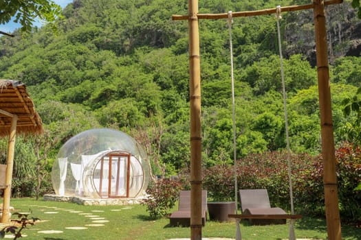 Romantic bubble house with transparent walls. White wooden double bed with mosquito net inside bubble. Honeymoon in an inflatable tent. Tourist attraction in tropical paradise on Bali, Indonesia