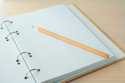 Pencil with open clear notepad on wooden table.