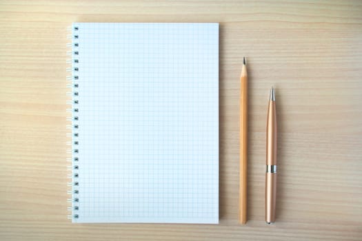Pencil and pen with open clear notepad on wooden table, copyspace.