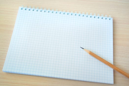 Pencil with open clear notepad on wooden table.