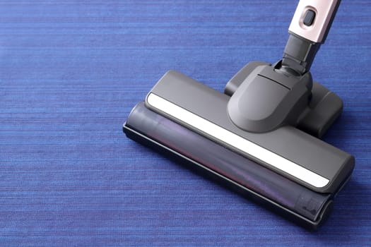Head of modern vacuum cleaner on blue carpet background. Close up.