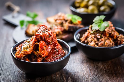 Sun dried tomato with olive oil as antipasto with tapenade and bruschetta in background