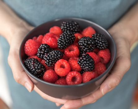 Female hands holding a bowl full of blackberries and raspberries.