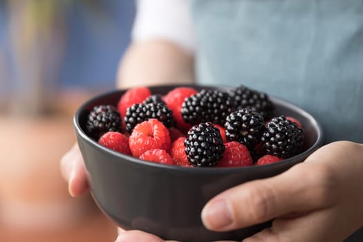 Female hands holding a bowl full of blackberries and raspberries.