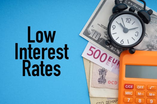 LOW INTEREST RATES text with alarm clock, banknotes currencies and calculator on blue background. Coronavirus Covid19 and Business Concept