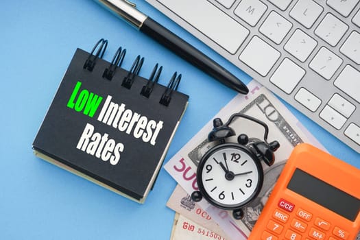 LOW INTEREST RATES text with keyboard, fountain pen, alarm clock, banknotes currencies and calculator on blue background.Coronavirus Covid19 and Business Concept