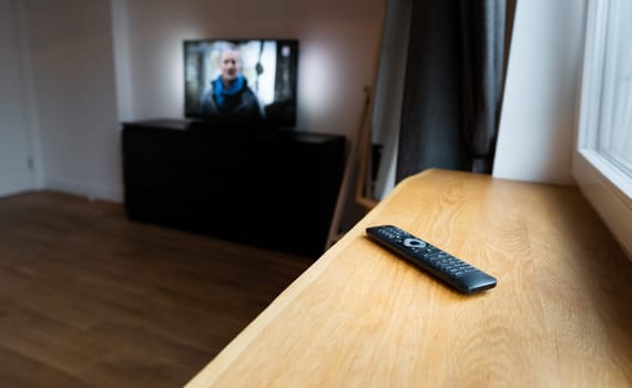 Remote Control for Wireless Smart Television, DVD, DVB-T2, K1, KI Plus, KII Pro, DVB-S2, Android TV Box, Set-Top Box, Satellite Receiver, HDTV, Media Player on wooden windowsill against TV background