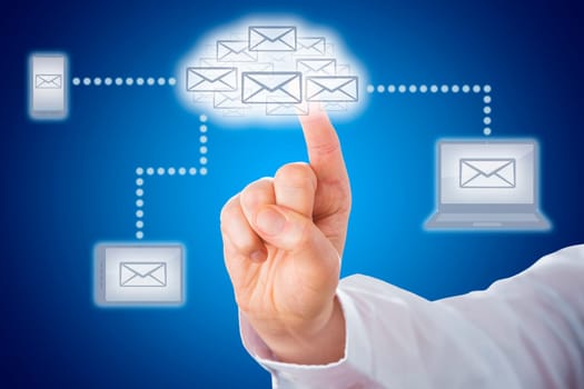 Host of email icons shaping a cloud symbol. The cloud computing icon does link to mobile devices that display a letter icon. Index finger of a business man is touching the cloud icon. Blue background.