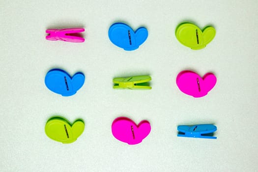 Colourful set of nine plastic clothespins or pegs on a light green sparkling background with copy field. View from above.
