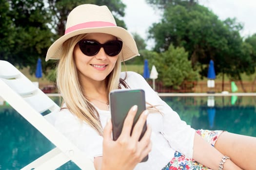 The attractive blond hair woman is using phone and making selfie about herself outdoors.