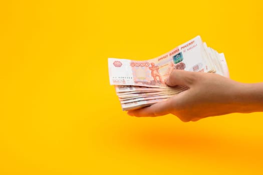 In hand a pack of five thousandth Russian rubles, yellow background