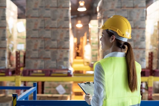 Side view of asian female warehouse worker with archboard flip chart look inventory with dustrubution warehouse in background. Reopening business warehouse technology and logistic concept.