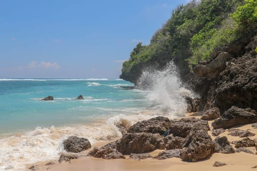 Pantai Gunung Payung beach with fine golden sand, Bali. Turquoise blue water turns into sea foam as the waves break against rocky cliffs of the coast. Sunny day with blue sky. Tourist natural concept.